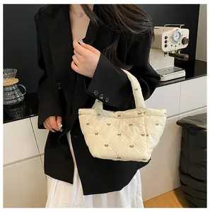 Close-up of cream quilted bucket bag with brown bow embroidery and sleek metal handle