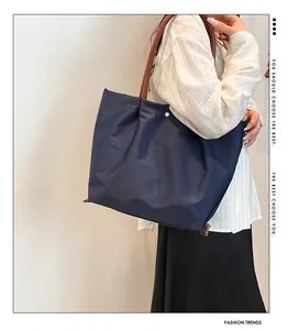 Detail showing deep blue nylon tote bag with brown leather handles and gold metal clasp
