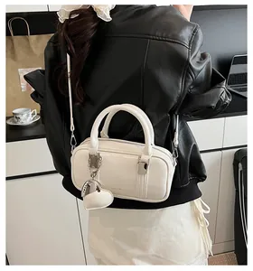 Close-up of cream Boston handbag with leather heart charm and adjustable strap