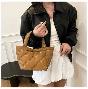 Detail of caramel brown quilted bucket bag featuring white bow embroidery and padded handle