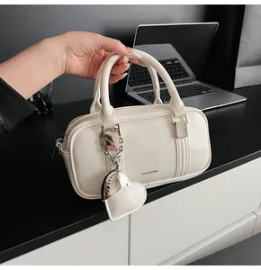 Detail of cream white boston bag featuring double handles and a leather heart pendant