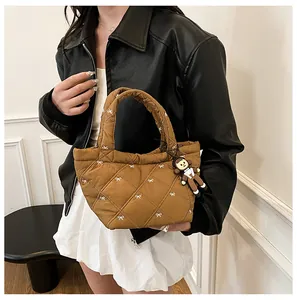 Detail of brown quilted tote bag with bow embroidery and cute doll pendant