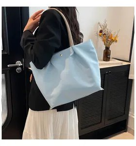 Close-up of light blue nylon tote bag with golden clasp and large capacity shown on shoulder