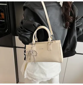 Stilvolle cremefarbene Baguette-Tasche mit Perlen-Schleife am Modell in modernem Ambiente