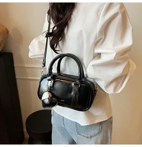 Detail of black glossy boston bag featuring a silver heart charm and metal chain accents