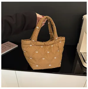 Detail of brown quilted bucket bag featuring white bow embroidery and padded handles