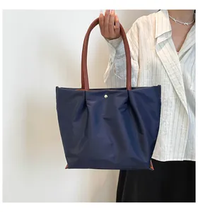 Detail view of large navy nylon tote bag with brown leather handles and gold snap button