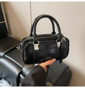 Close-up of black Boston bag with glossy finish and silver buckles on leather background