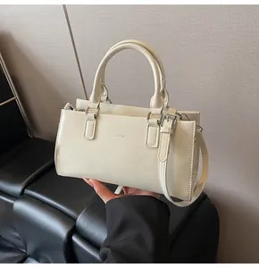 Detailansicht der cremefarbenen Ledertasche mit silbernem Logo und Schultergurt