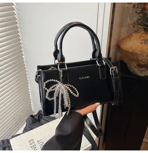 Detail der schwarzen Kunstledertasche mit weißem Logo und Perlen-Schleifen-Anhänger
