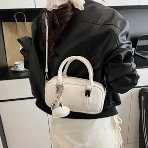 White glossy Boston bag with heart charm and shoulder strap shown in a lifestyle view