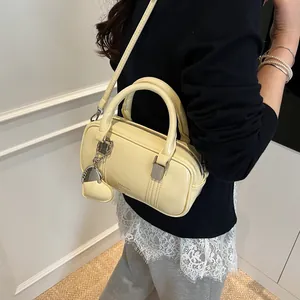 Cream yellow faux leather Boston bag with heart charm and top handles in casual studio setting