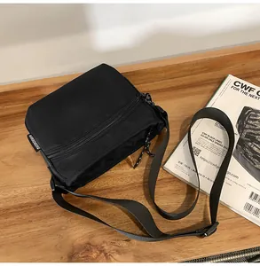 Close-up of a black nylon crossbody bag with zipper pockets on a wooden table with magazines
