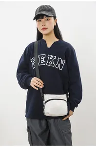 Detail of a minimalist off-white nylon crossbody bag with black zipper on model