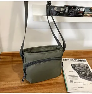 Olive green nylon crossbody bag featuring a front zipper pocket on a wooden tabletop