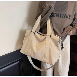 Close-up of minimalist cream travel bag worn as a crossbody by model in natural setting