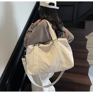 Side view of a large beige duffel bag worn by a model in a modern staircase setting