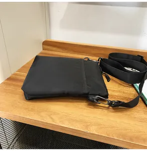Detail of black nylon messenger bag with matte hooks on a natural wooden table