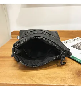 Close-up of black nylon shoulder bag with multiple zippered compartments on wooden surface