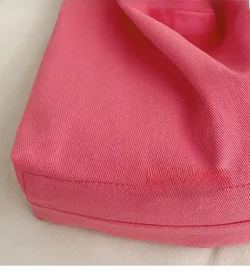 Close-up of durable rose red canvas fabric with clean stitching on a minimalist tote bag