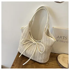 Vue détaillée d'un sac cabas en paille avec nœud en cuir sur table en bois rustique