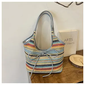 Détail du sac cabas rayé en paille avec un nœud en cuir gris et une texture rustique
