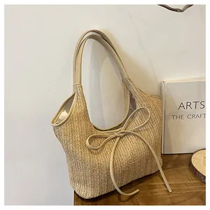 Détail d'un sac cabas en paille tressée avec garniture en similicuir crème et nœud