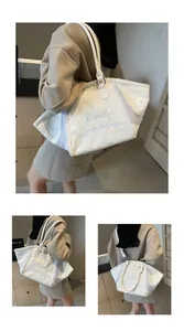 Detail of white tote bag with black cursive embroidery and adjustable shoulder strap