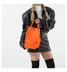 Close-up of bright orange felt tote bag featuring embossed cross detail and mini pouch