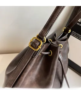 Close-up of vintage dark brown faux leather bucket bag with gold metal buckle and texture
