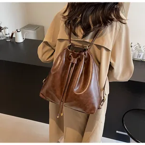 Detailed back view of a brown leather drawstring bucket backpack on a model's shoulder