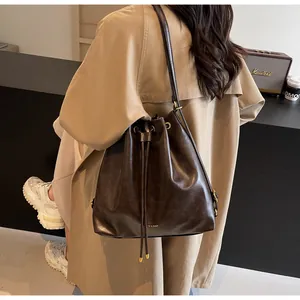 Detail of dark brown leather bucket bag with drawstring closure worn with a beige trench coat
