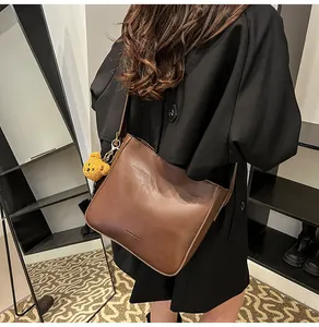 Détail d'un sac seau vintage en cuir marron foncé avec un porte-clés ours en peluche jaune