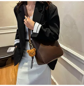 Détail du sac bandoulière vintage en cuir marron avec breloque d'ours en peluche