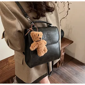 Dettaglio di uno zaino vintage in pelle PU nera con un ciondolo a forma di orsetto