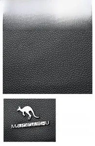 Detail of black pebbled leather texture with a metallic kangaroo logo and chain strap