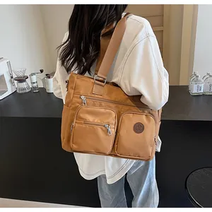 Detail of tan canvas tote bag showing three front zipper pockets and leather logo patch
