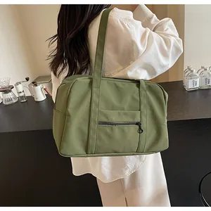 Minimalist olive green nylon travel tote bag shown on a woman's shoulder in a lifestyle setting