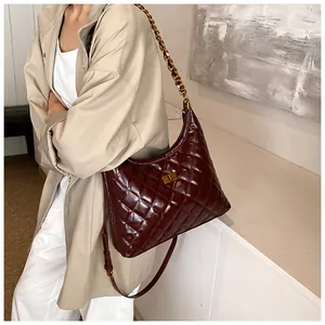Detail of dark red quilted saddle bag with glossy finish and gold chain strap