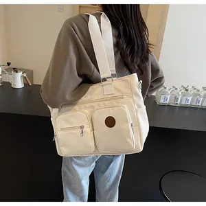 Close-up of a large beige nylon tote bag featuring functional zippers and a leather patch