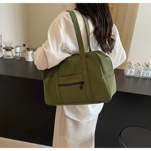Detail view of a large green nylon tote bag carried on a shoulder in a cafe setting.