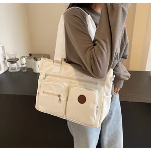 Detail of off-white canvas tote bag featuring two front zipper pockets and logo patch