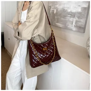 Detail of burgundy quilted saddle bag with gold chain and glossy leather texture
