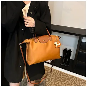 Detail view of large orange tote bag with leather flap and horse charm accessory