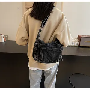 Close-up of washed black denim crossbody bag with multiple zippers and wide strap
