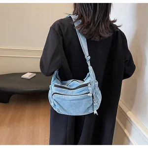 Detail of light blue washed denim crossbody bag with dual zipper pockets on model
