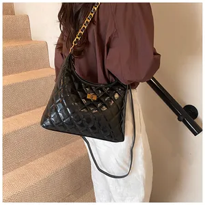 Detail of black quilted saddle bag with gold metal clasp and woven chain strap on model