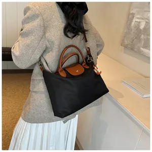 Detail of black nylon tote bag with leather handles and an orange fox charm on model