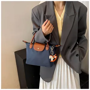 Detail of dark blue nylon tote bag with brown leather handles and a horse charm