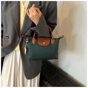 Detail of green nylon tote bag featuring brown leather trim and orange doll pendant